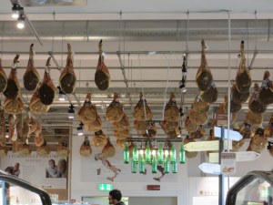 Prosciutti hang from the ceiling at the top of a moving ramp leading to the salumi department.