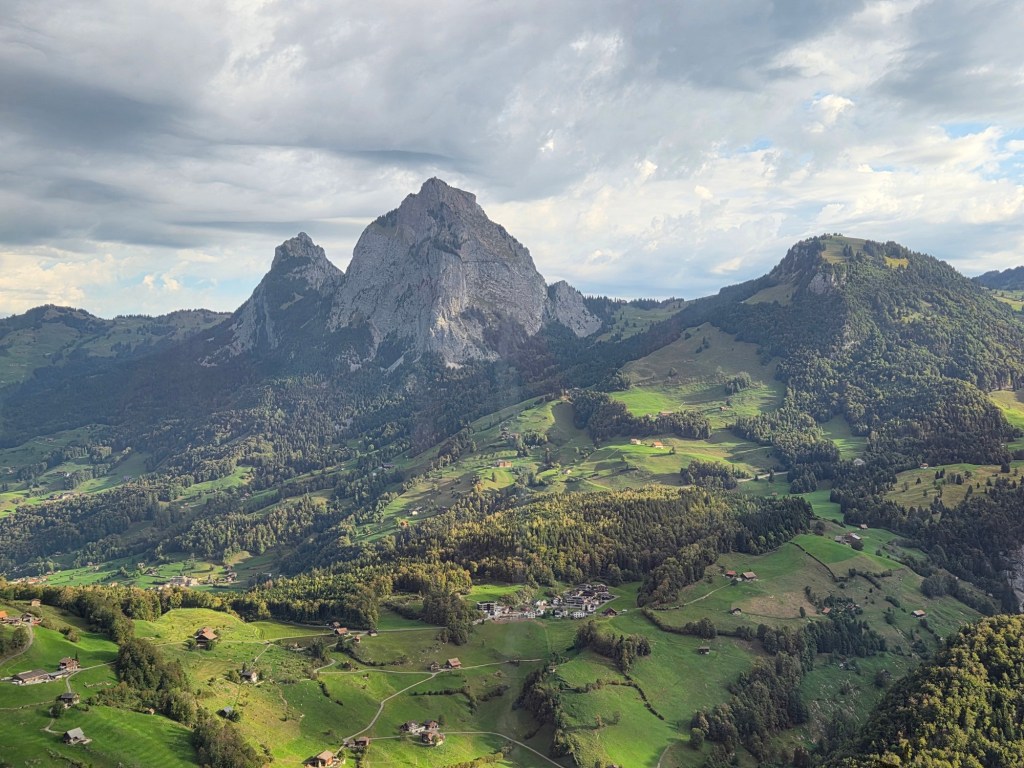 A scenic view of mountains surrounded by lush green valleys and small houses in a picturesque landscape.